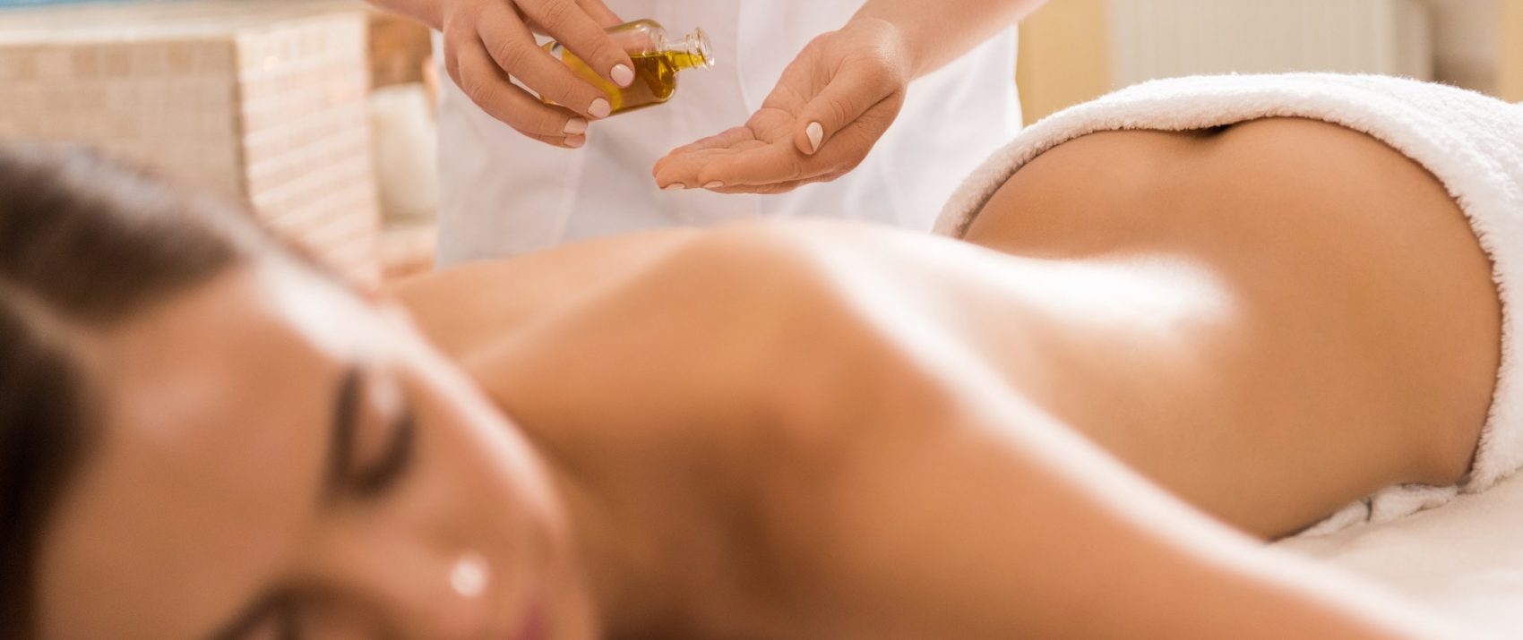 massage therapist making massage with body oil for woman in spa salon